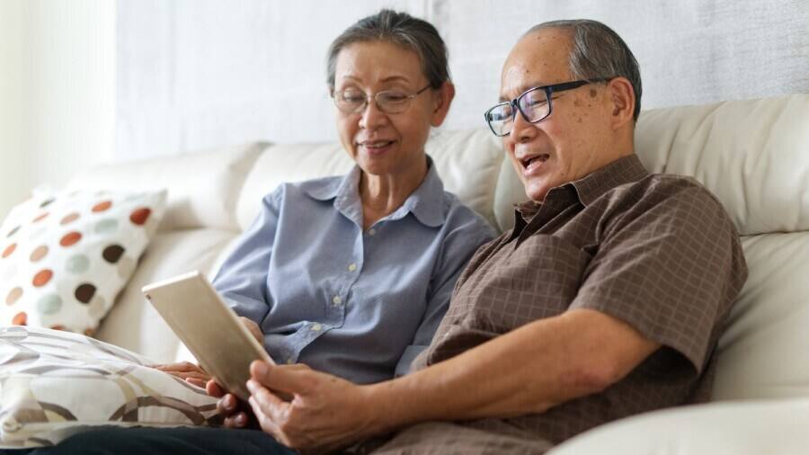 aged couple sitting on a sofa with a table reading