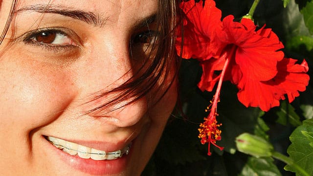 Mujer sonriendo al lado de una flor roja