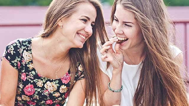 Gülümseyen ve atıştırmalık yiyen iki kadın