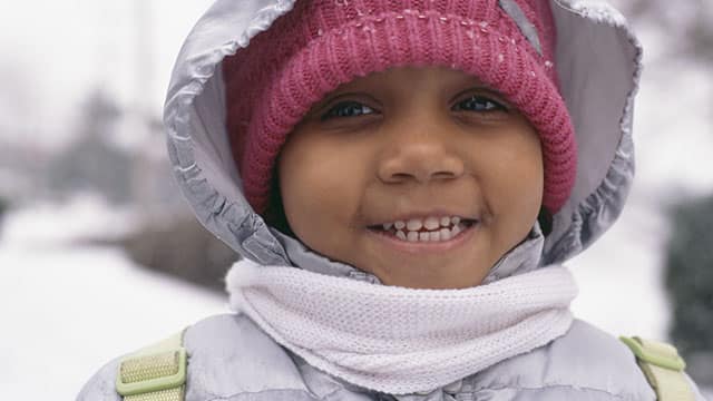 Niña muy abrigada sonriendo bajo la nieve