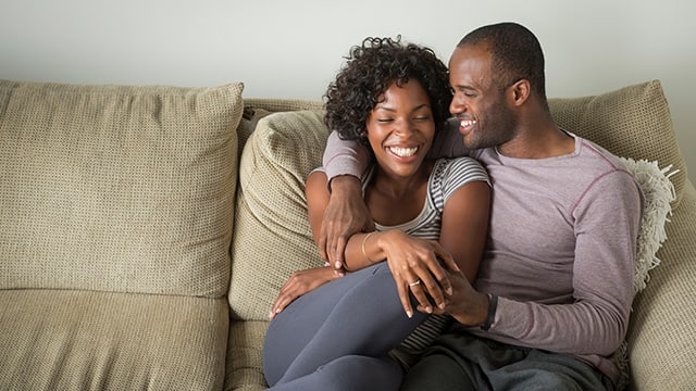 A happy couple relaxing together on a sofa, sharing a joyful moment and smiling.