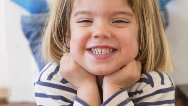 Niña sonriendo sosteniendo su cabeza con las manos