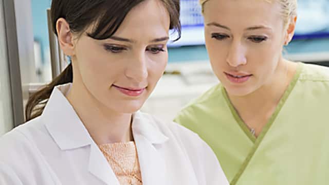 Nurse in green scrubs looking over dentists shoulders