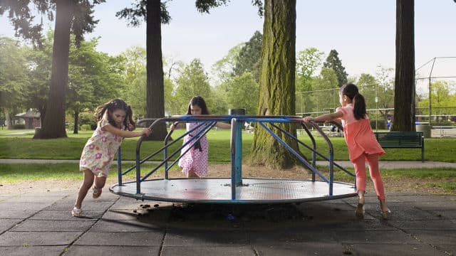 three girls running around a merry go round at the playground