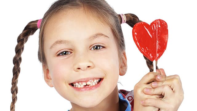 A girl with missing baby teeth is holding a lolipop