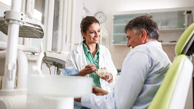 Female dentist in dental office talking with senior male patient while preparing for treatment