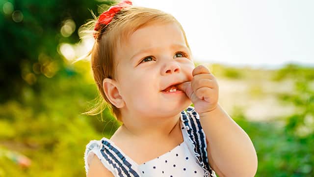 The little girl with short hair is sucking finger while looking up in an outside setting