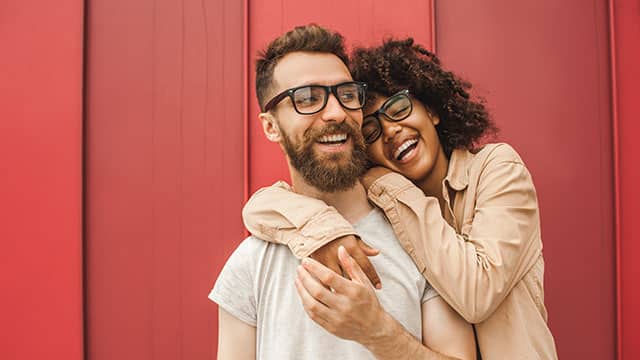 A happy young couple in eyeglasses smiling and hugging on the street