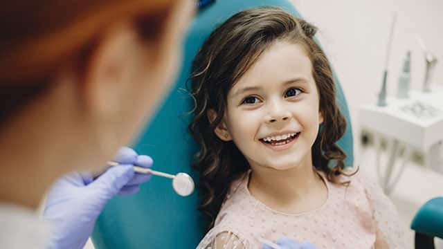 Little kid smiling while talking with the pediatric dentist after doing a tenth examination in a pediatric somatology