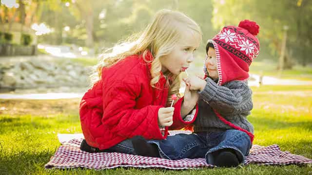 Little Girl with Baby Brother enjoying lollypops Outdoors