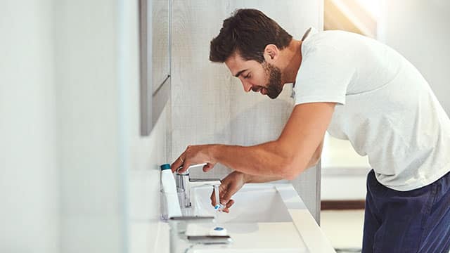A man is washing his toothbrush in a bathroom