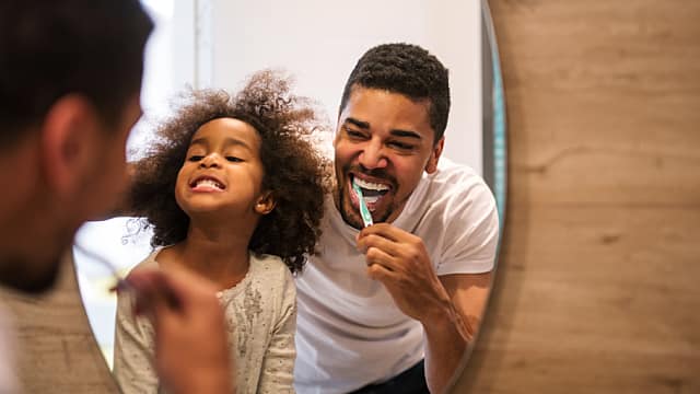 Father and daughter are brushing their teeth over the sink