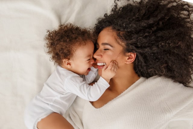 mother and baby laying down in bed next to each other smiling