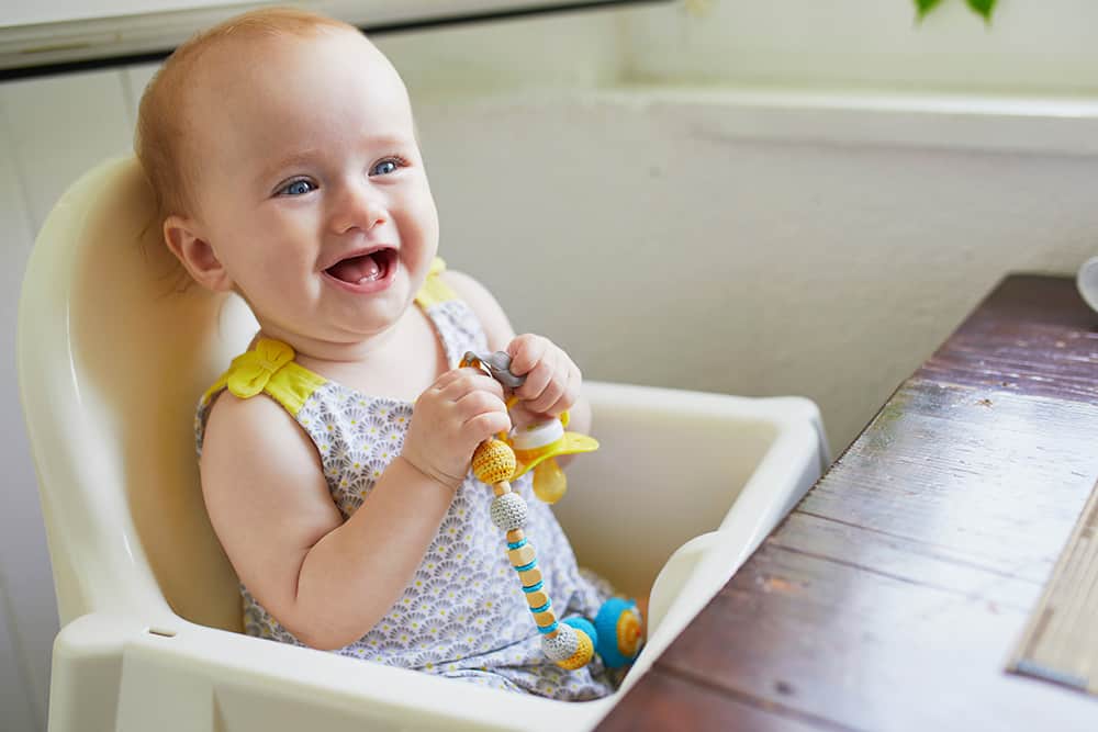 Little baby girl sitting in a high chair holding a pacifier
