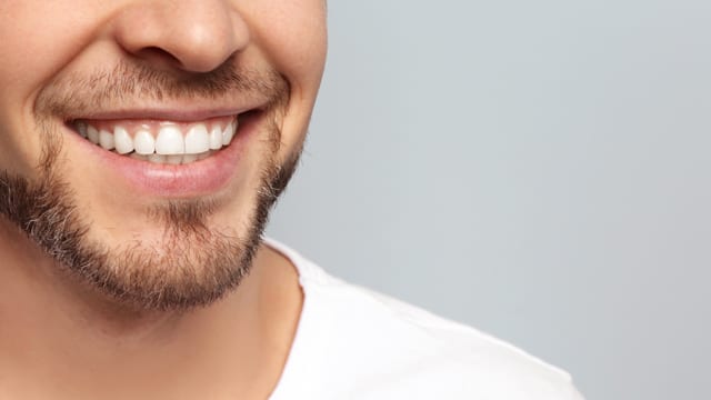 Close-up of a young man smiling in front of a gray wall