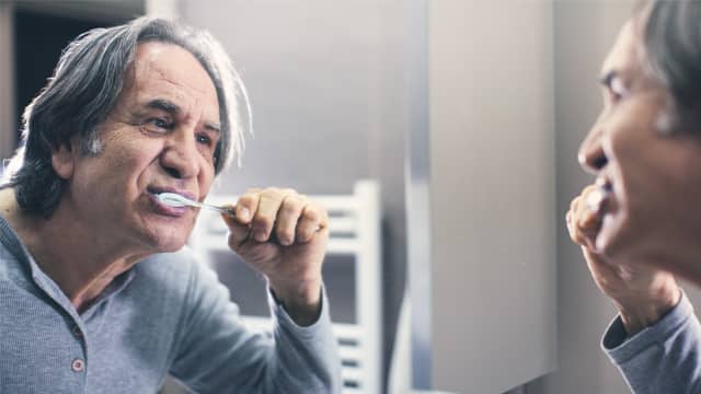 Senior man brushing his teeth in a bathroom mirror