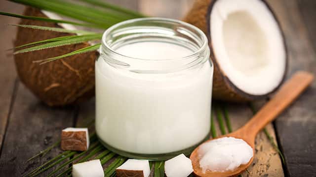 Coconut oil in a jar surrounded by two real coconuts on a wooden table