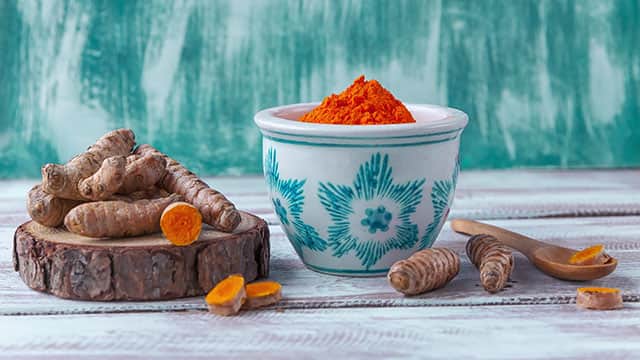 Turmeric powder in a bowl and Turmeric roots on a wooden table.