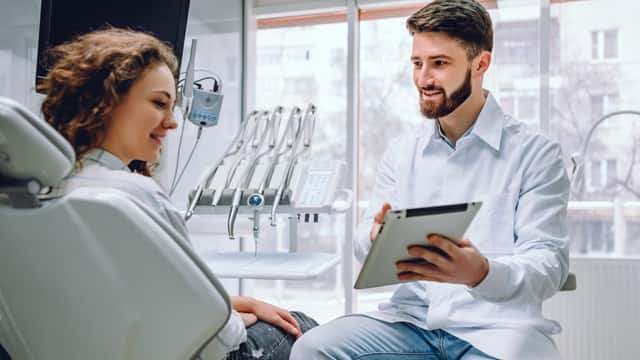 A male dentist discussing results with a female patient using a tablet in a dental office