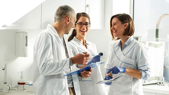 Dentist team of three in a dental office talking and smiling 