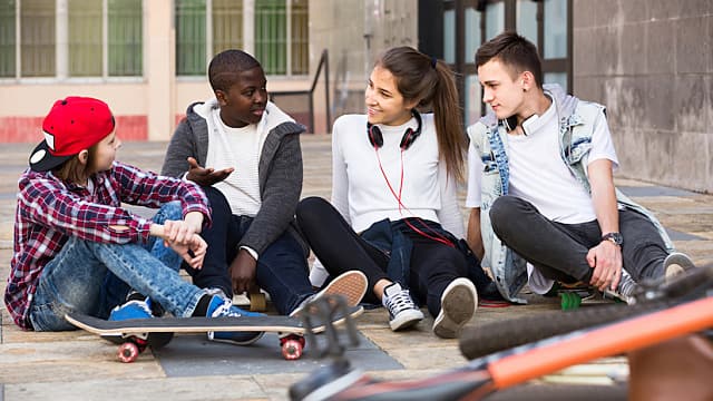 Girl And Three Boys Hanging Out Outdoors And Discussing Something 