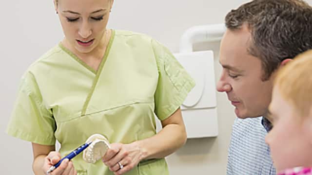 Dental hygienist using mouth model to explain what's on the monitor screen to young patient and their parent