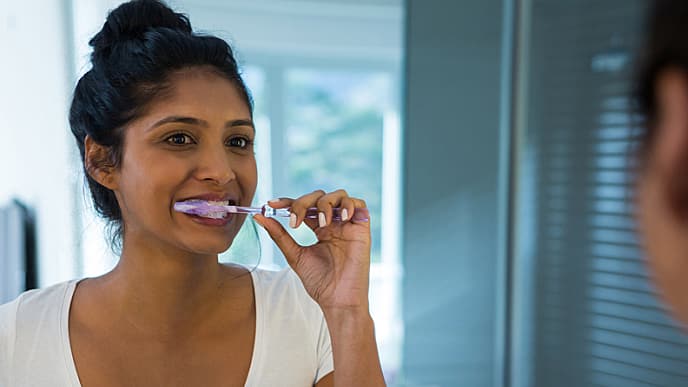 Woman brushing and having thoughts on how to stop gum bleeding while looking in the mirror  