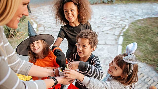 Children in Halloween costumes trick or treating with an adult handing them candy