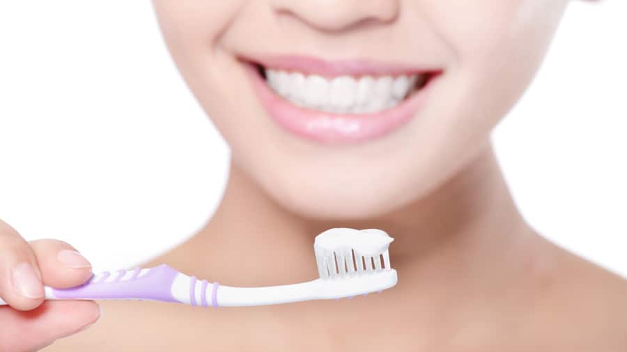 Close-up of a young woman smiling while brushing her teeth, using a stannous fluoride toothpaste for strong enamel protection