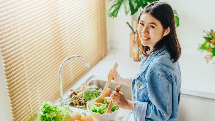 Smiling woman mixing salad, promoting healthy habits to reduce bacteria in mouth 
