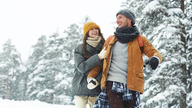 A beautiful young couple in puffy jackets holding hands and laughing while enjoying winter stroll