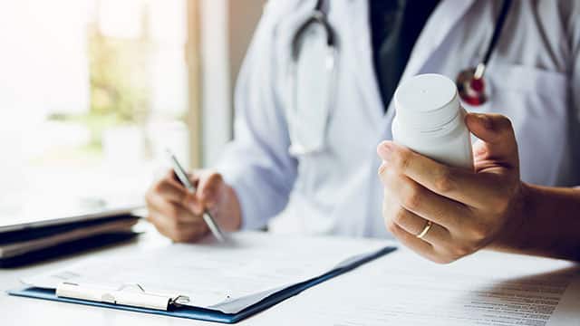 doctor holding a bottle of pills and writing a prescription.