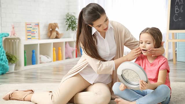 a mother holding her daughter cheeks while she is looking at a mirror