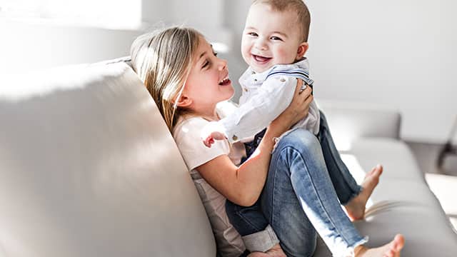 Little sister with her baby brother having good time at home while sitting on the sofa 