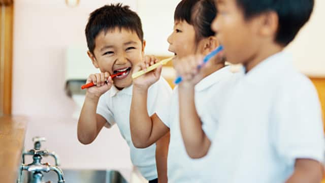 Three cute kids brushing their teeth in front of a mirror.