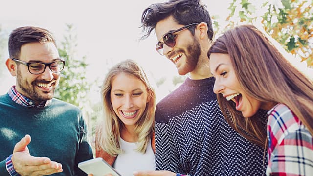 Happy smiling young friends walking outdoors in the park holding smart phone.