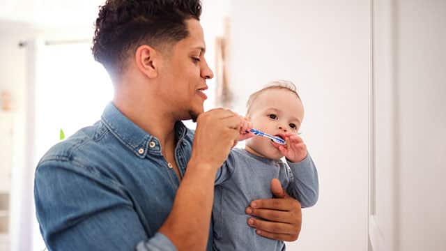 Father and his small toddler son in a bathroom brushing their teeth