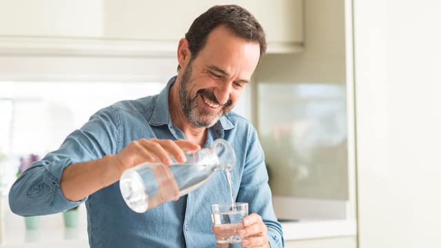Hombre sirviéndose agua en un vaso mientras sonríe