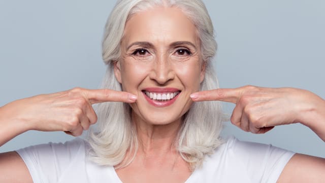 A older woman smiling and pointing to her teeth