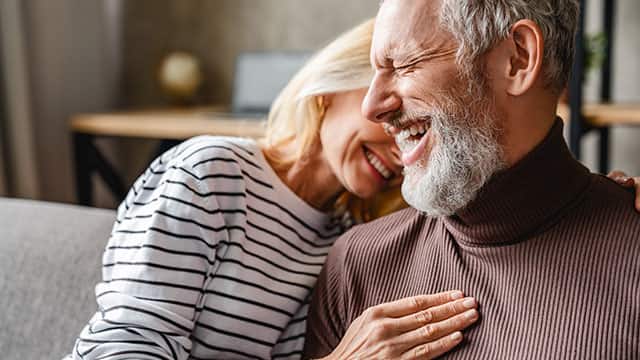 A happy laughing middle aged couple embraced while sitting on a sofa