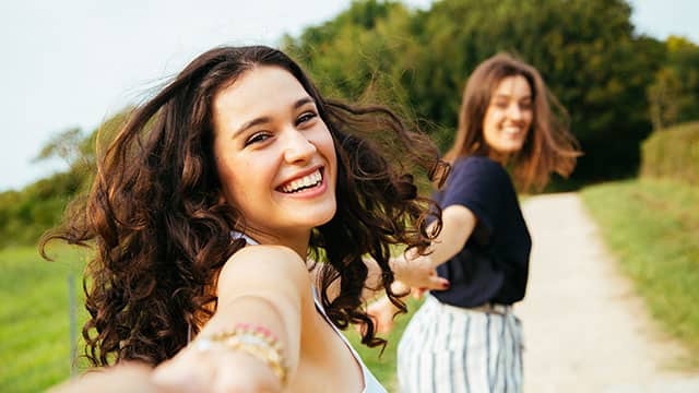 Two girls with bright white smiles running and smiling while holding hands