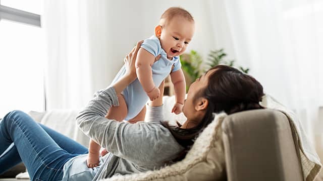 Young woman lying on a sofa while holding a baby