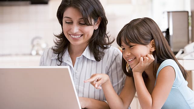 Woman and young girl in kitchen with laptop and paperwork smiling