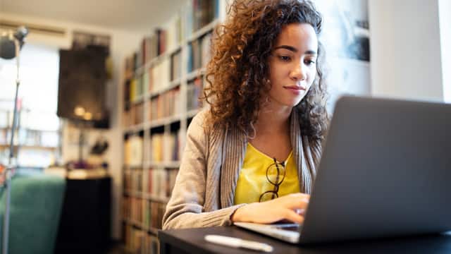 Young woman with curly hair doing research on a laptop at home