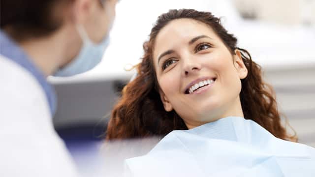 A female patient lying in a dental chair talking to a male dentist