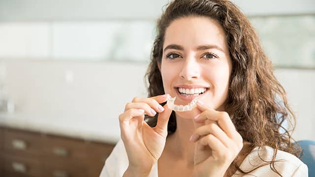 A female patient is holding orthodontic retainer in dental clinic