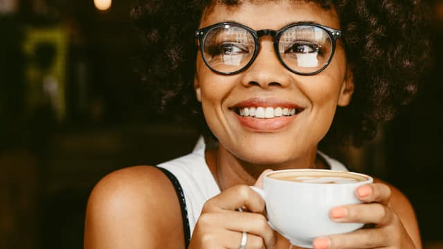 Young woman in glasses drinking coffee in a cafe