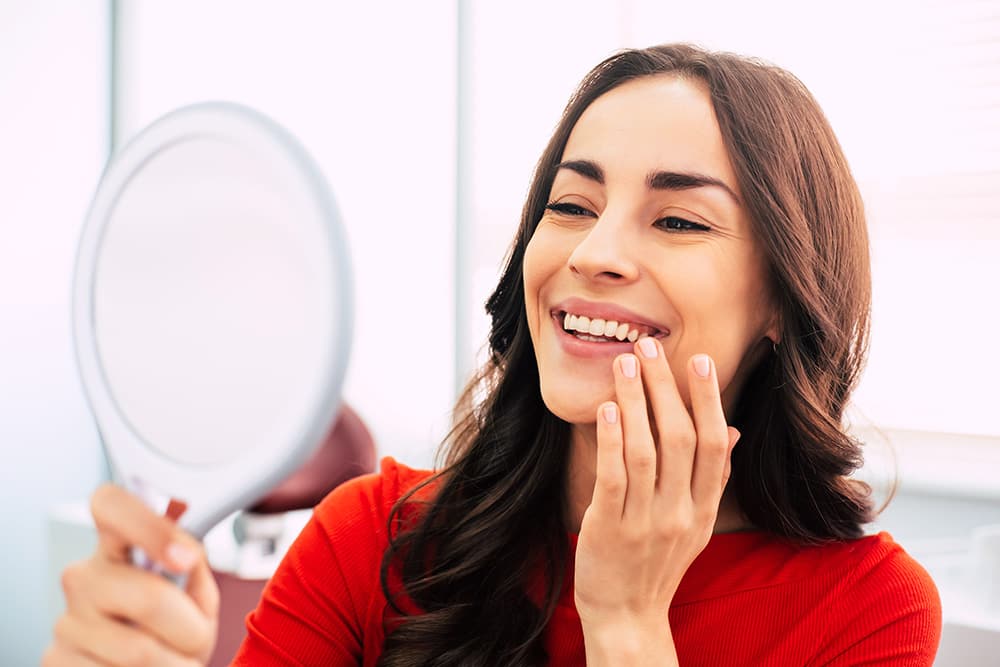 A woman is looking at her teeth in the mirror