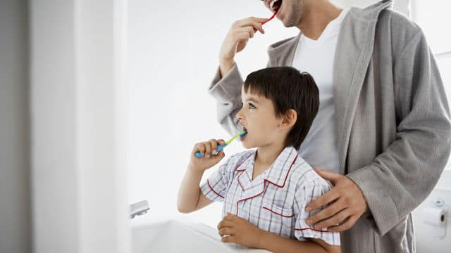 baba ve çocuk aynaya bakarken colgate diş macunu ile birlikte fırçalıyor