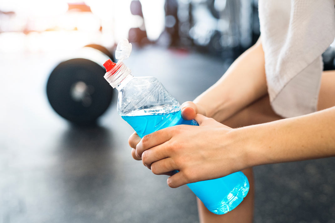 Athlete holding a plastic bottle of blue sports drink during a gym workout break